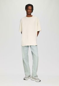 Crème oversized t-shirt gecombineerd met lichtblauwe straight-leg jeans en grijze sportschoenen, met een minimalistisch ontwerp en een relaxte pasvorm.