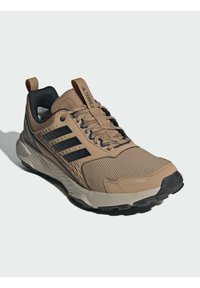 Beige athletic shoe with black accents, textured mesh upper, cushioned sole, and a pull tab, designed for outdoor activities.