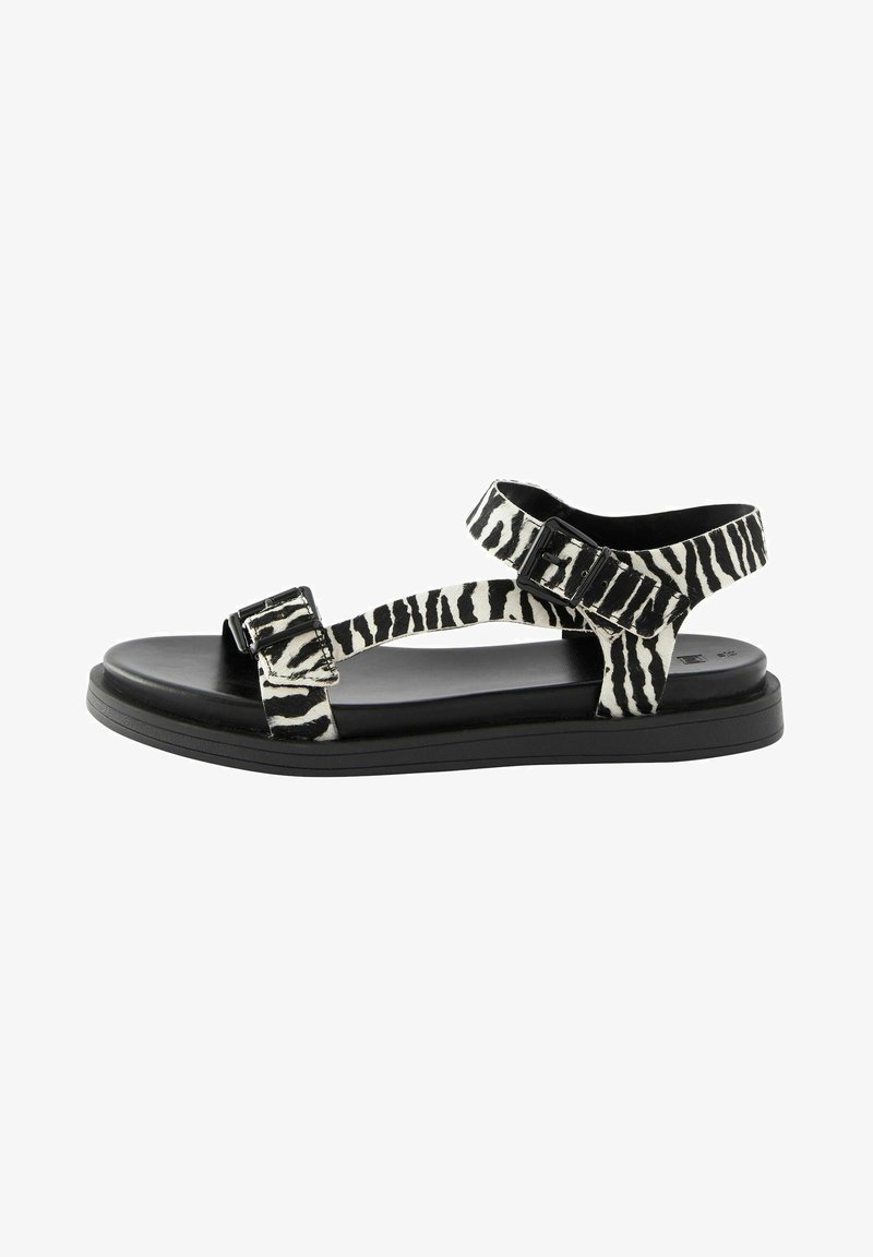 Sandales imprimé zèbre noir et blanc avec deux boucles ajustables, semelle plate noire et design à bout ouvert. Matériau léger et brides texturées.