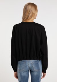 Felpa nera cropped con maniche lunghe, colletto a costine e vita elasticizzata, abbinata a jeans in denim azzurro chiaro con tasche posteriori.