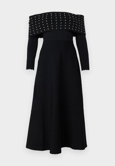 Crna haljina bez naramenica s dugim rukavima, rebrastom teksturom, valovitim rubovima i srebrnim zakovicama duž izreza i tijela.