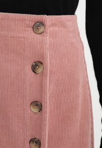 Gonna di velluto a coste rosa con righe verticali, caratterizzata da tre grandi bottoni lucidi sul davanti e un dettaglio sulla vita.