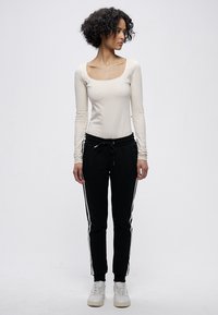 Krēmkrāsas garroku tops ar apaļu izgriezumu, komplektā ar melnām biksēm ar baltām sānu svītrām un elastīgu vidukli. Valkāts ar baltām sporta kurpēm.