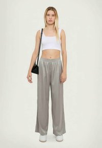 Graue Satin-Hosen mit weitem Bein und elastischem Bund, kombiniert mit einem weißen, cropped Tanktop und weißen Sneakers. Eine schwarze Schultertasche ist ebenfalls enthalten.