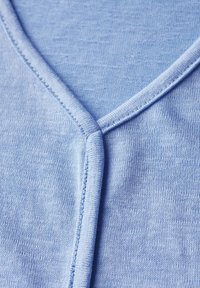 Haut bleu clair à col en V fabriqué en tissu doux et texturé. Il présente un décolleté soigneusement cousu et une finition lisse sur le corps.
