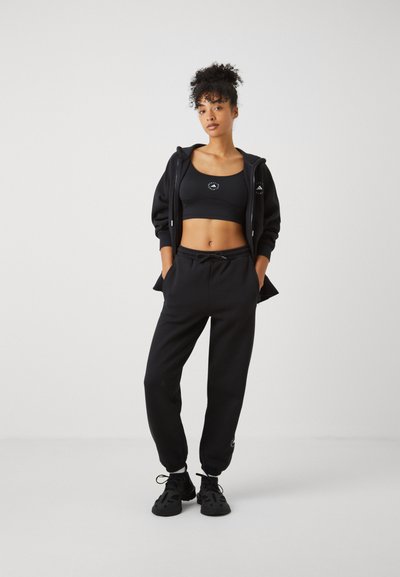 Black athletic outfit featuring a cropped sports bra, zip-up hoodie, and loose joggers. Material appears soft with a smooth texture.