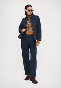 Μπλε τζάκετ από τζιν με αντίθετο γιακά, πορτοκαλί και καφέ ρίγες ζιβάγκο, και παντελόνι φαρδύ σε ναυτικό μπλε χρώμα, συνδυασμένο με μποτάκια από βαμβάκι βουργουνδίας.