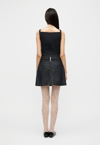 Μαύρο κοντό τοπ και σκούρα φούστα από τζιν, συνδυασμένα με ανοιχτόχρωμες καλσόν με δαντελωτό σχέδιο. Διαθέτει κλείσιμο με φερμουάρ και μινιμαλιστικό σχέδιο.