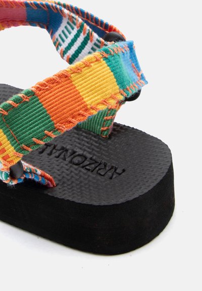 Κοντινό πλάνο ενός μαύρου πλατφόρμας σανδάλι με υφή στη σόλα και πολύχρωμες ριγέ υφασμάτινες λουρίδες που συγκρατούνται με μαύρα κουμπιά.