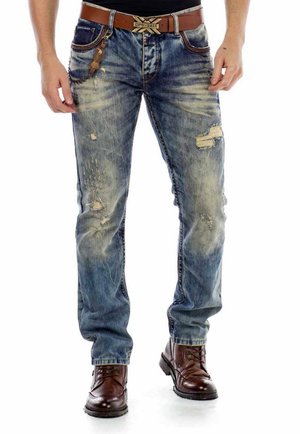 Blaue Jeans aus Denim mit distressed Details und verblassten Stellen, getragen mit einem braunen Ledergürtel und braunen Schnürstiefeln.