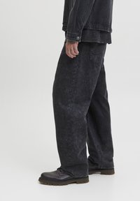 Sorte denimbukser med en falmet tekstur, løs pasform og synlig syning. Sammen med mørke, snøre-støvler og en sort jakke.