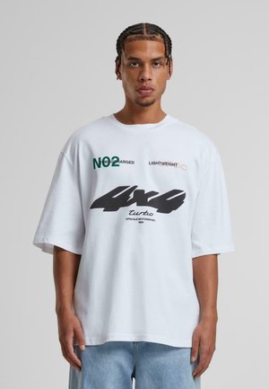 Hvid oversized t-shirt med sort og grøn trykt tekst og grafik. Bemærkelsesværdige elementer inkluderer "4x4 turbo" og "NO² CHARGED" designs.