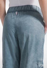 Jasnoniebieskie spodnie cargo wykonane z miękkiego materiału, z elastycznym paskiem w talii, bocznymi kieszeniami i fakturowanym wykończeniem. Minimalne oznaczenia marki.