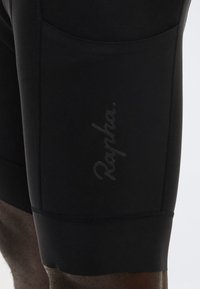 Κοντινό πλάνο μαύρων σορτς ποδηλασίας με διακριτικό λογότυπο «Rapha» τυπωμένο στον μηρό, που δείχνει την υφή του υφάσματος και τις λεπτομέρειες της ραφής.