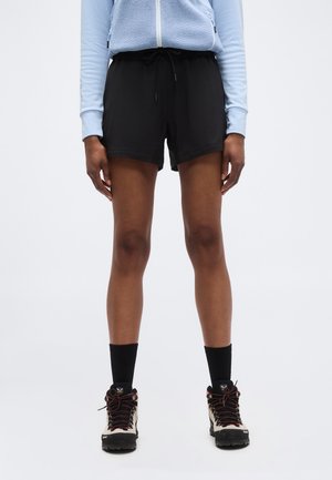 Person wearing black drawstring shorts, black mid-calf socks, beige and black hiking boots, and a light blue long-sleeve top with a zipper.