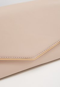 Světle růžové kožené psaníčko s geometrickým tvarem, zdobené zlatavým akcentem podél okraje a viditelnými stehami.