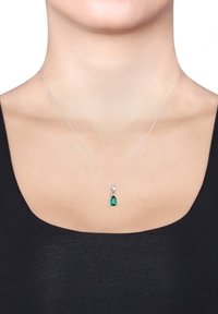 Hõbedast kaelakee, millel on teardrop-kujuline smaragdist ripats, millel on paljastoode pind, rippumas õhukeselt kettilt.