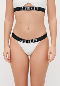 Ensemble de bikini côtelé blanc avec une bande élastique noire portant le logo "CALVIN KLEIN". Le design met l'accent sur le confort et une esthétique minimaliste.