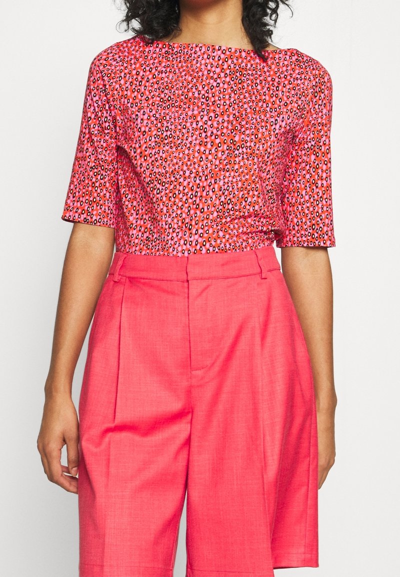 Krátký rukáv top v jasně růžové látce s puntíkovaným vzorem, spojený s vysokými růžovými šortkami s sklady a hladkou texturou.