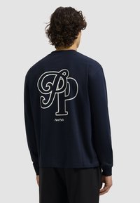 Marineblauwe longsleeve shirt van katoen met een groot wit "PP" logo en de tekst "PurePath" op de achterkant. Eenvoudig, minimalistisch ontwerp.