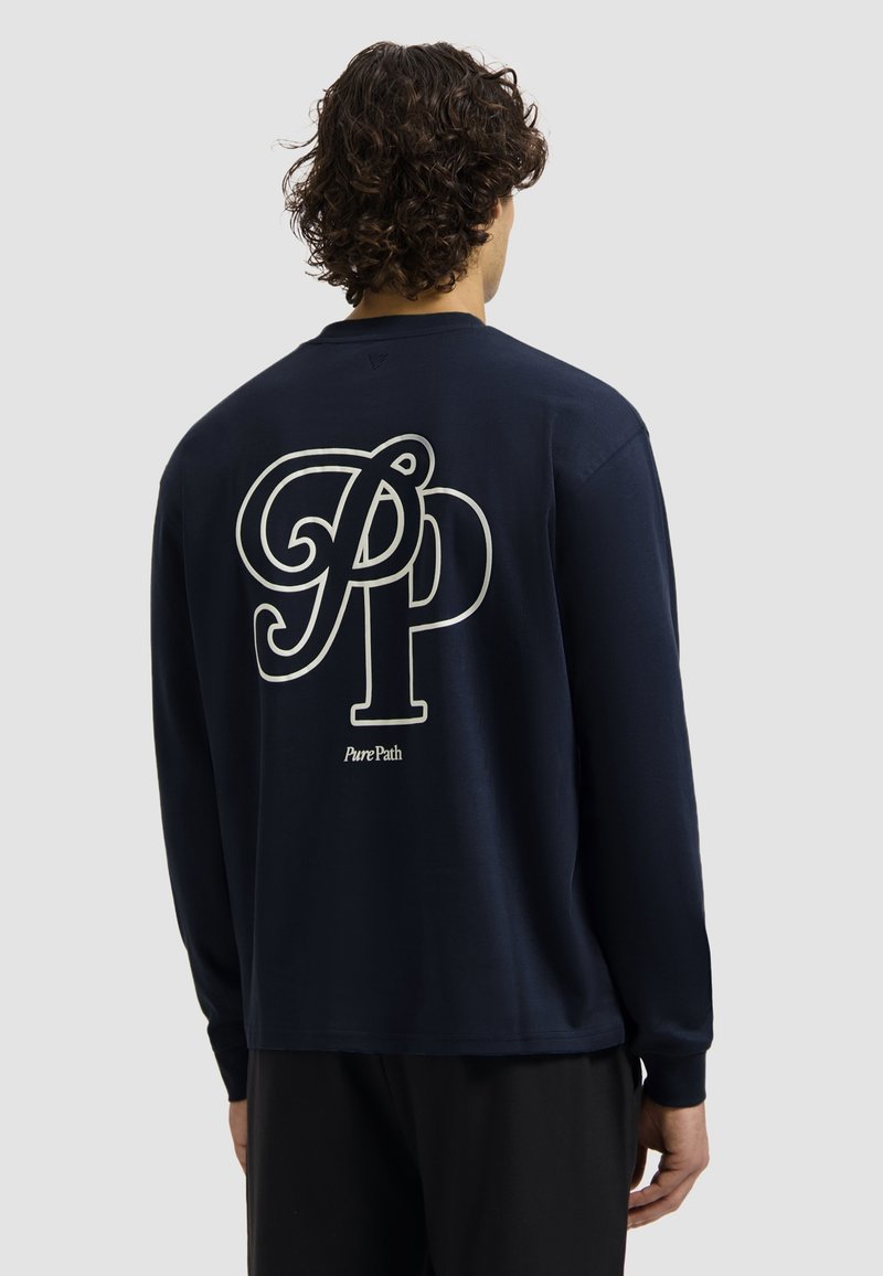 Marineblauwe longsleeve shirt van katoen met een groot wit "PP" logo en de tekst "PurePath" op de achterkant. Eenvoudig, minimalistisch ontwerp.