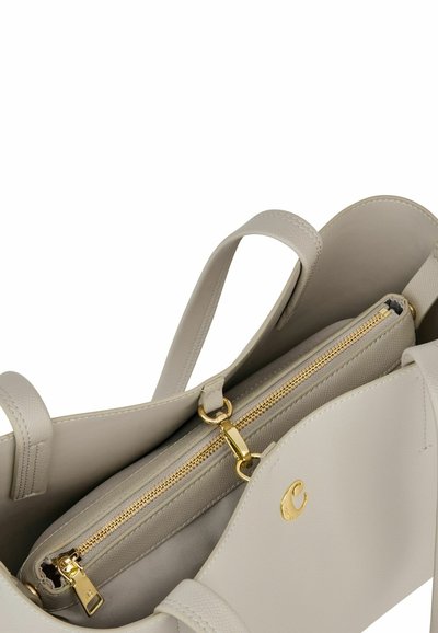 Bež usnjena torba za prenašanje z dvema ročajema, zlatim zadrgo in majhnim zlatim logotipom na sprednjem žepu.