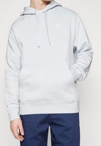 Ljusblå Nike-huvtröja i mjukt material, med en framficka, justerbara dragkedjor och en vit logotyp på bröstet.