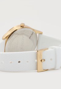 Λευκό λουράκι ρολογιού με υφή και χρυσή πόρπη που φέρει λογότυπο κροκόδειλου, προσαρτημένο σε ρολόι με χρυσή θήκη και πίσω μέρος από ανοξείδωτο ατσάλι.