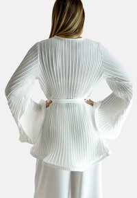 Weißes, plissiertes Oberteil mit langen Glockenärmeln und taillierter Taille, aus glattem Material gefertigt, mit vertikalen Streifen und Rundhalsausschnitt.