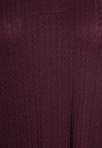 Burgundy stickad tyg med en strukturerad mönstring av vertikala linjer och chevronformer, som skapar ett subtilt, lager-på-lager utseende.