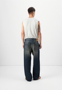 Denim spijkerbroeken met een losse pasvorm, donkerblauwe kleur en een vervagings effect op de benen. Voorzien van twee achterzakken en een leren label bij de taille.