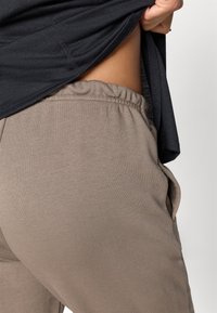 Beige joggebukser med elastisk midje og sidelommer, kombinert med en svart skjorte som delvis er hevet, og viser en glatt hudtone.