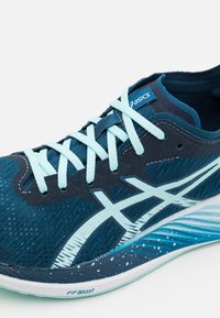 Chaussure de course Asics bleu foncé avec lacets bleu clair, logo latéral et semelle à motif intitulée FF Blast, présentée sur fond blanc.