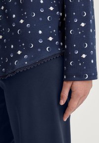 Top blu navy con motivo celestiale che include lune e pianeti; presenta un bordo in pizzo all'orlo. Abbinato a pantaloni blu navy uni.