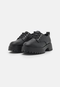 Chaussures noires en cuir avec un bout arrondi et une semelle crantée épaisse. Comprend un style à lacets, des œillets en métal et une languette au talon.