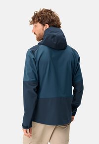 Veste imperméable bleu marine avec capuche, présentant des manches sombres contrastées et une texture lisse. Manches ajustables et coupe moderne.
