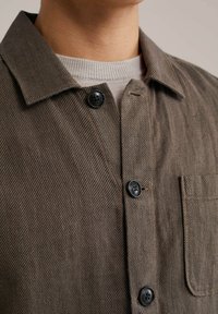 Button-up shirt in brown herringbone fabric, featuring a classic collar, chest pocket, and black buttons with a textured finish.