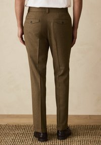 Brown checkered trousers with a slim fit, two back pockets, and a textured fabric. Worn with a white shirt and black shoes.