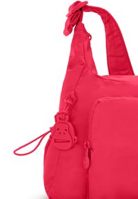 Lys pink skuldertaske lavet af nylon med en glat overflade. Har en frontlomme og et silikone nøgletræk formet som en abe.
