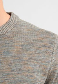 Maglione lavorato a maglia con un motivo texturizzato e multicolore nelle tonalità di grigio, blu e arancione. Presenta un collo rotondo a coste e una cucitura sulle spalle.