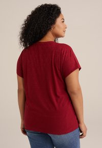 T-shirt rosso con motivo a fantasia fogliare, maniche corte e orlo arrotondato, abbinato a jeans in denim blu.