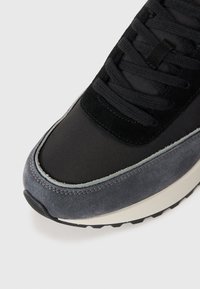 Zwarte en grijze sneaker van suede en nylon materiaal, ronde neus, gevoerde tussenzool, gestructureerde buitenzool en contrasterende stiksels.