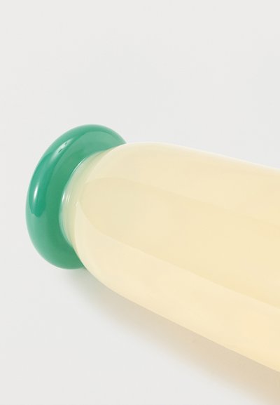 Διαυγής γυάλινο μπουκάλι γεμάτο με ωχρό κίτρινο υγρό, σφραγισμένο με πράσινο στρογγυλό καπάκι, εμφανίζεται με φόντο ένα απλό φωτεινό φόντο.