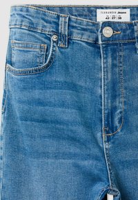 Niebieskie dżinsy w fasonie z przemysłowym praniem, z przednią kieszenią, miedzianymi szwami oraz metalowym zapięciem na guzik. Metka zawiera informacje o rozmiarze.