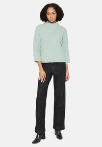 Jasnoniebieski, teksturowany sweter dziany z wysokim kołnierzem i rękawami do łokcia, zestawiony z czarnymi, szerokimi spodniami jeansowymi oraz czarnymi botkami na obcasie.