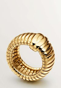 Pulsera de metal dorado con un diseño acanalado y acentos suaves, que crea una apariencia texturizada. Su forma circular permite un uso fácil.