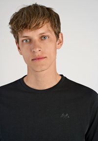 Mustapaitapaita, joka on valmistettu pehmeästä kankaasta ja jossa on hienovarainen harmaa vuoristologotipo vasemmassa rinnassa. Yksinkertainen, istuva muotoilu.