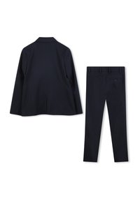 Granatowa marynarka i dopasowane spodnie zwężane. Marynarka ma klapę z wycięciem; spodnie posiadają cztery kieszenie i pojedyncze zapięcie na guzik.