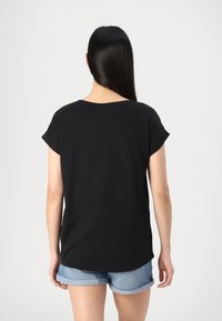 T-shirt noir à manches courtes avec col rond, fabriqué en tissu léger ; doté d'une coupe décontractée et d'un ourlet arrondi. Porté avec un short en denim.