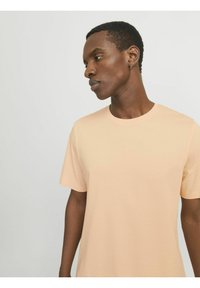 Camiseta de algodón en color durazno claro con cuello redondo y mangas cortas, que presenta una textura suave y un corte casual.